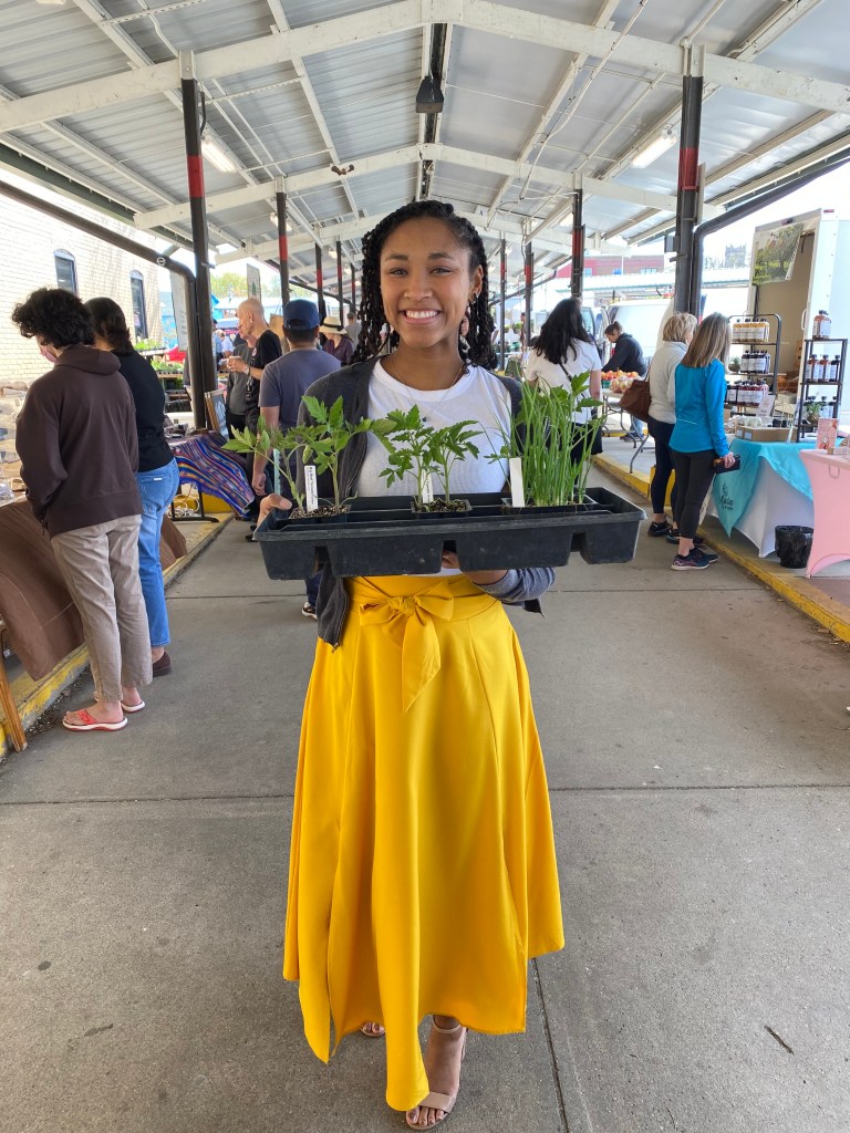 Blair holds a tray of new plants for her garden. She's wearing a golden yellow skirt.